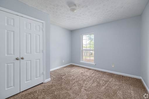 A room with a carpeted floor, a window, and a white door.