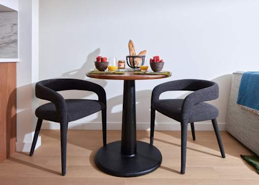 A round table with two chairs and a bowl of fruit on it.