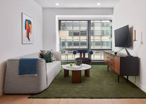 A living room with a grey couch, a coffee table, a flat screen TV and a window overlooking a city.