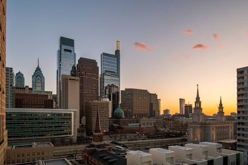 A city skyline at sunset with tall buildings and a church steeple.at 1600 Callowhill, Philadelphia Pennsylvania