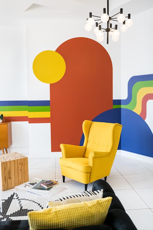 A yellow chair is in front of a colorful wall.
