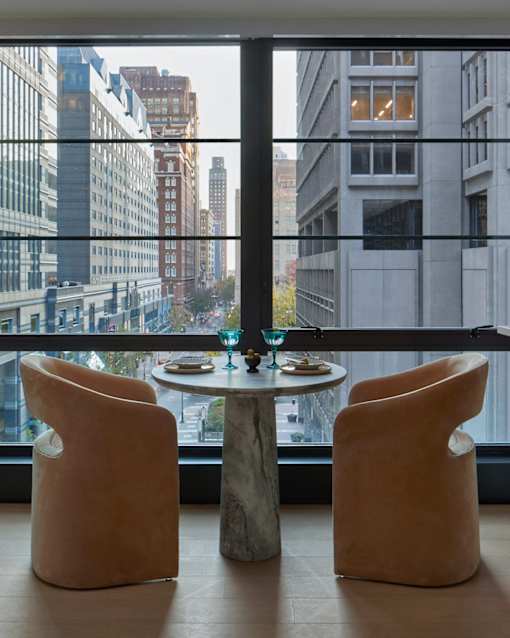 Two tan chairs are placed in front of a table with a view of the city.