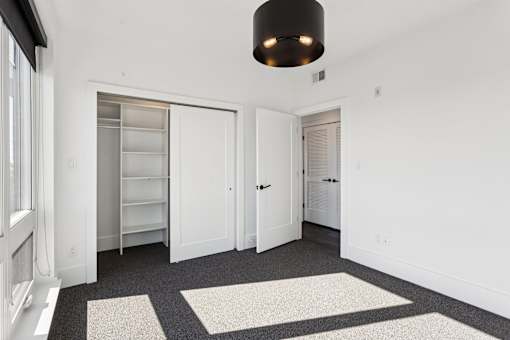 A white room with a black ceiling light and a grey carpet.