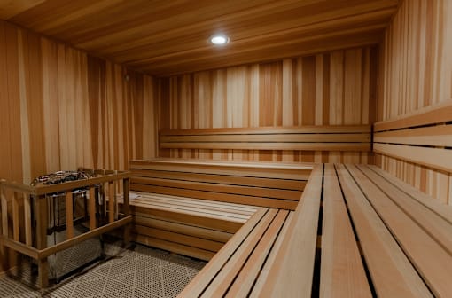 A wooden sauna with benches and a stone container on the left at The Hawthorn