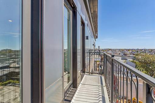 A balcony with a metal railing and glass doors overlooking a cityscape.