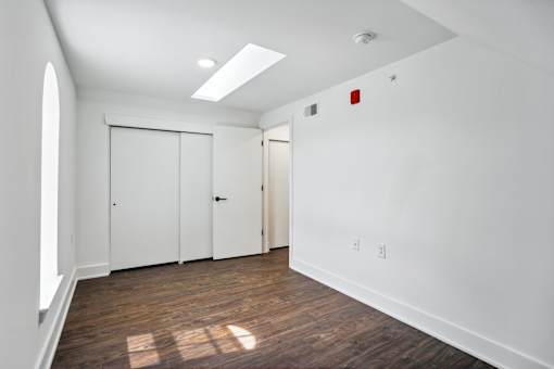 A room with white walls and wood flooring with a skylight.