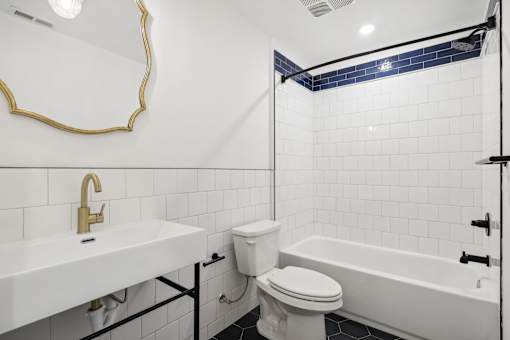 A white bathroom with a gold faucet and a white toilet.
