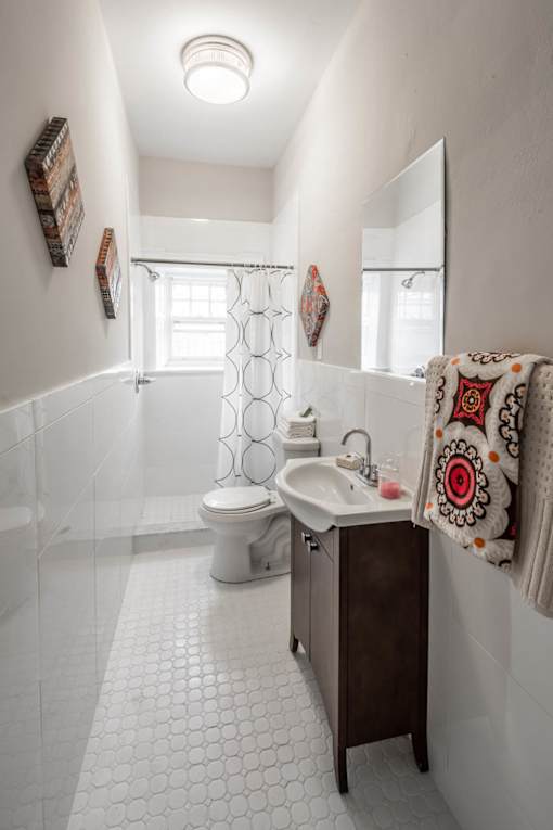 A white tiled bathroom with a toilet, sink, and mirror.