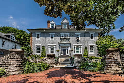 A large, grey house with a stone wall and steps leading to the front door.