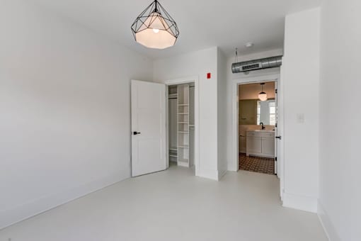 A white room with a light hanging from the ceiling and a doorway leading to another room.