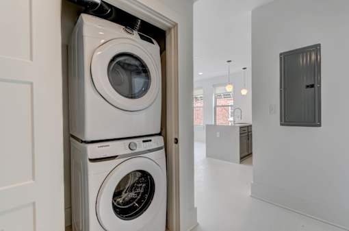 A white washing machine is stacked on top of another white washing machine in a laundry room.