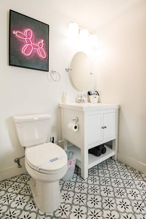 A white toilet with a pink neon sign above it.