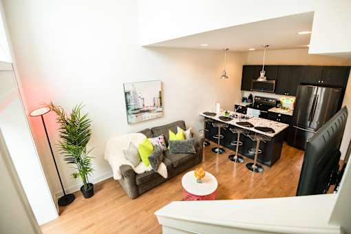 A modern kitchen with a black fridge and stove, a dining table with chairs, and a living area with a couch and a potted plant.