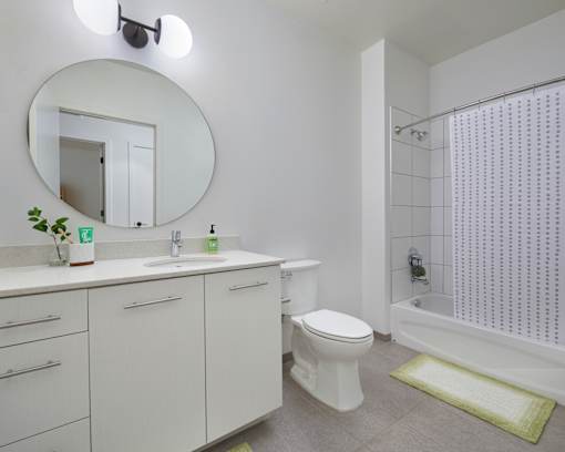 A white bathroom with a round mirror and a green rug. at 1600 Callowhill, Philadelphia, PA