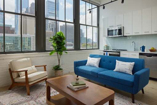 A blue couch with white pillows sits in a living room with a view of the city. at 1600 Callowhill, Philadelphia, PA