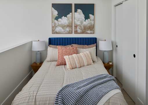 A bed with a blue headboard and a white comforter with a blue and white checkered blanket on it. at 23 West Apartments, Philadelphia, PA