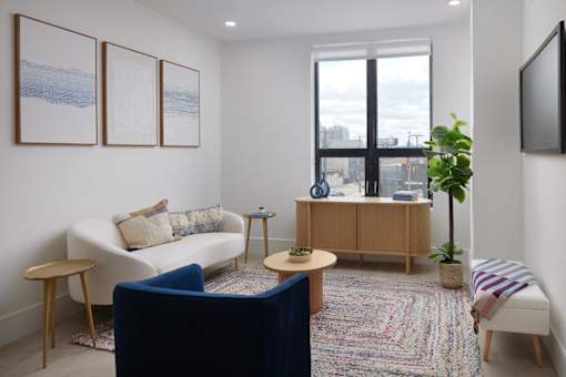 A living room with a white couch, a blue chair, a wooden cabinet, and a flat screen TV mounted on the wall.