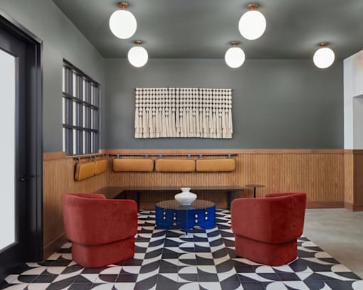 A black and white checkered floor in a room with a wooden bench and red chairs. at The Weaver, Philadelphia, PA, 19125