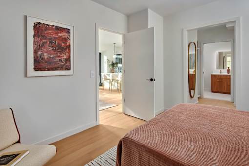A bedroom with a red bedspread and a painting on the wall.