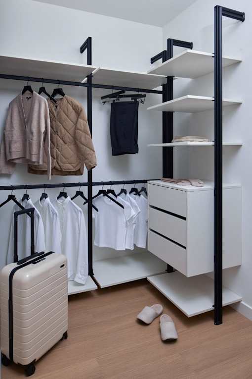 A white closet with clothes and a suitcase.
