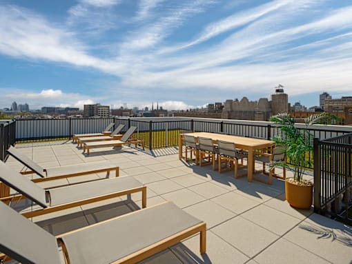 A rooftop patio with tables and chairs overlooking a city skyline.