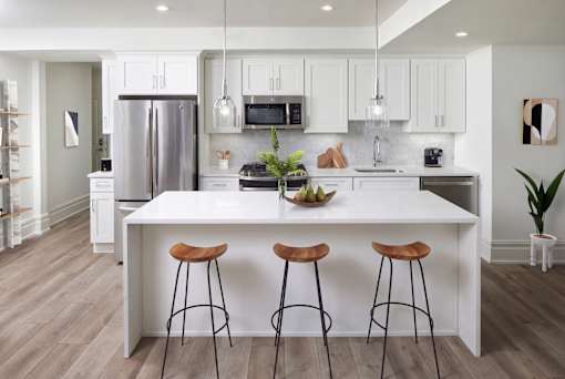 A modern kitchen with white cabinets and a large island with three stools.