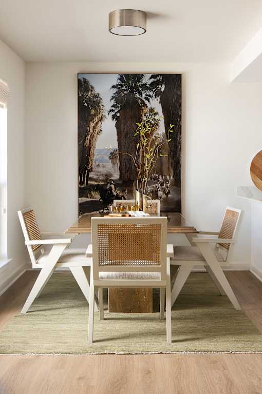 A dining room with a table set for two and a large painting of a palm tree in the background at The PARKER on E Mulberry Apartments, Texas