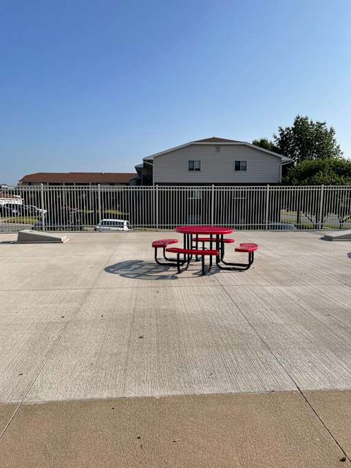 A picnic table with a red top is in the middle of a concrete area.