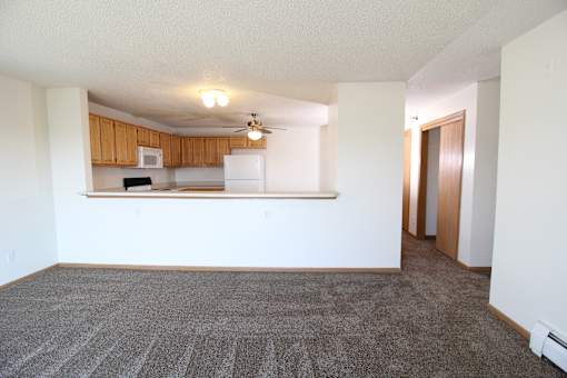 an empty living room with a kitchen in the background