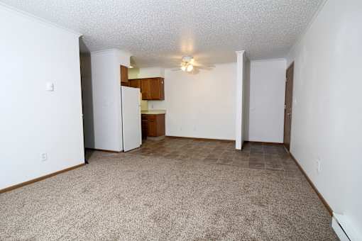 an empty living room with a kitchen in the background