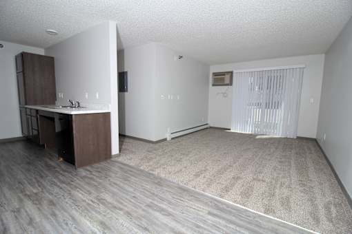 an empty living room with a kitchen in the background