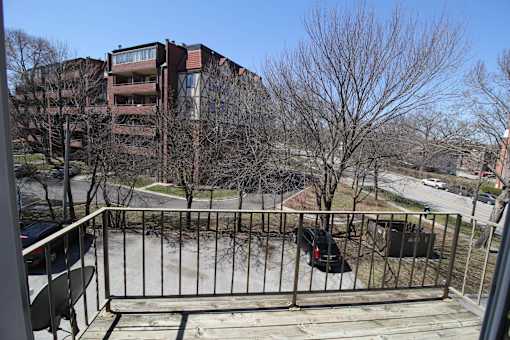 A balcony with a metal railing and a tree in front of a brick building.