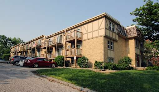 A red car is parked in front of a building with a balcony.