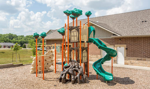a playground with a slide and climbing equipment in front of a brick building