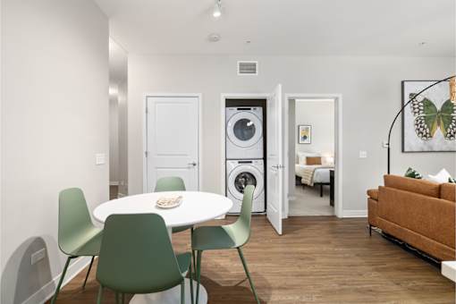 A white table with green chairs is in a room with a washing machine in the background.