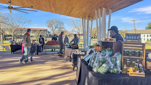 A group of people are standing around a table with bags of produce on it.