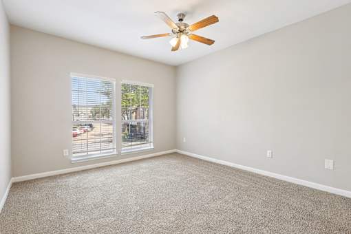 A room with a ceiling fan and a window overlooking a parking lot.
