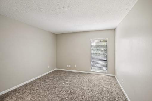 A room with a carpeted floor and a window with blinds.