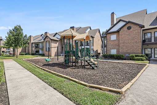 A playground with a green slide and a brown gravel area in front of a row of houses.