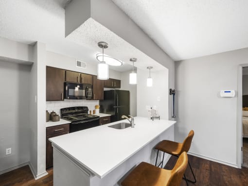 a kitchen with a white counter top and a white island with a sink and two chairs