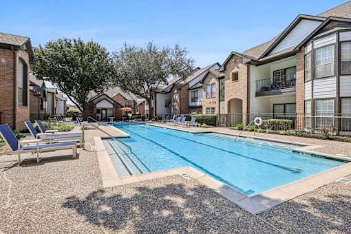 A swimming pool surrounded by apartment buildings and lounge chairs.