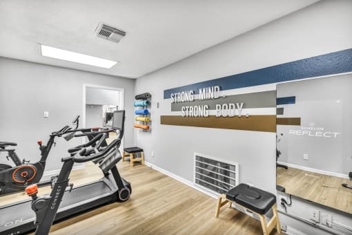 the gym with a reformer exercise bike and a wall with a sign that reads