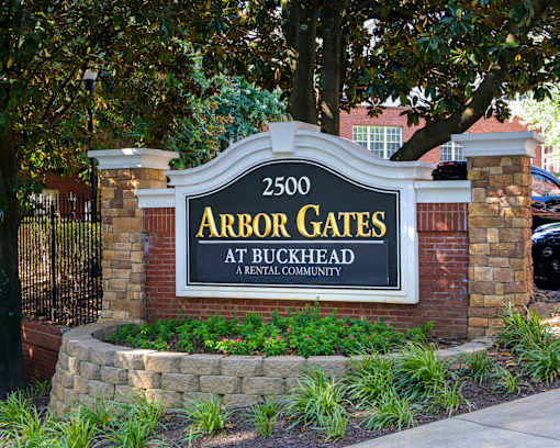 A sign for Arbor Gates at Buckhead, a rental community, is displayed in front of a brick wall and trees.