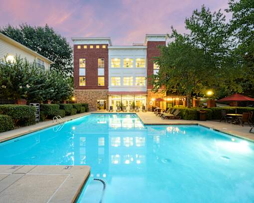 A large swimming pool in front of a building with a red umbrella and chairs around it.
