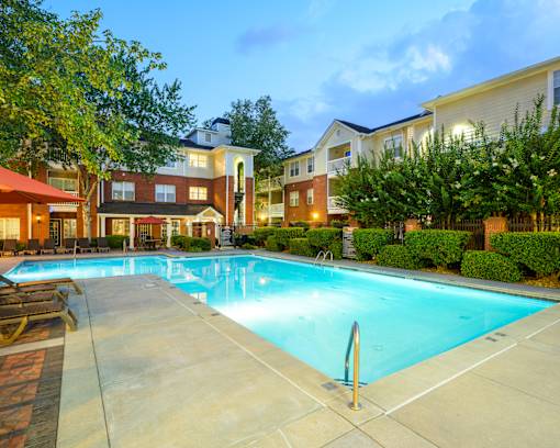 A large swimming pool surrounded by a concrete patio and residential buildings.