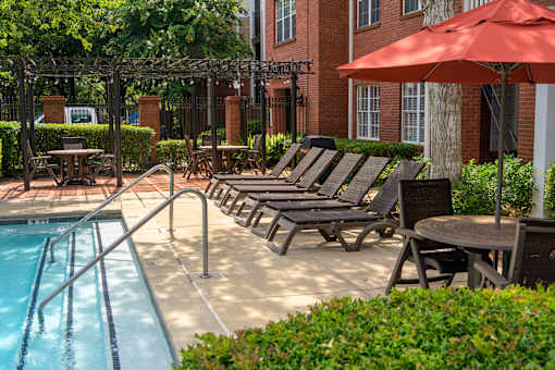 A pool with a red umbrella and chairs around it.