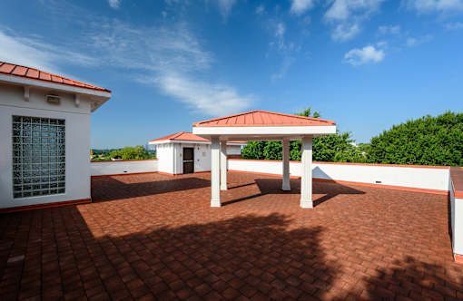 A patio with a red roof and a white building with a window and a door.