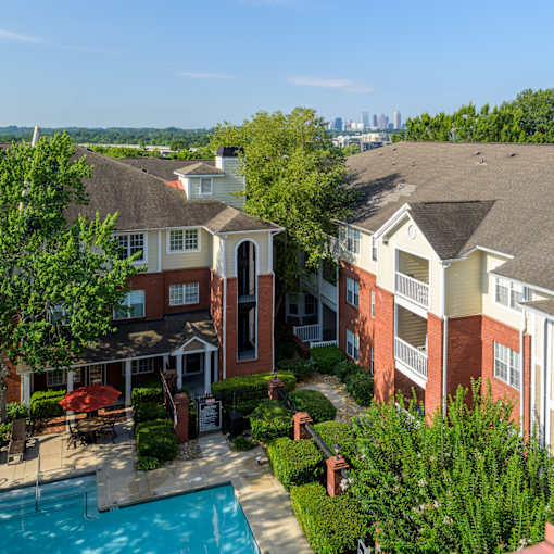 A swimming pool is surrounded by a patio and bushes in a residential area.
