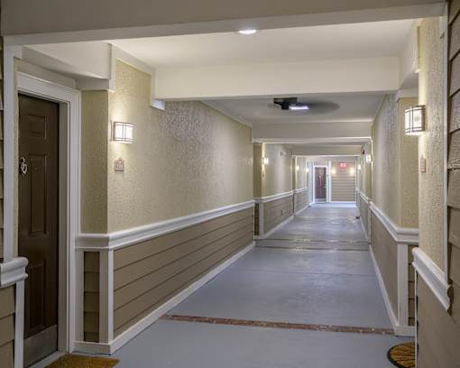 A long hallway with a light on the wall and a fan on the ceiling.