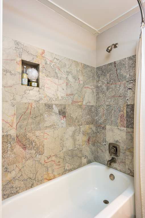 A bathroom with a marble wallpaper and a white bathtub.